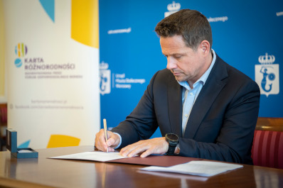 Zdjęcie. Prezydent Rafał Trzaskowski siedzi przy biurku i podpisuje kartę różnorodności 